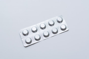 Full package of silver tablets lying vertically diagonally on a uniform light gray background