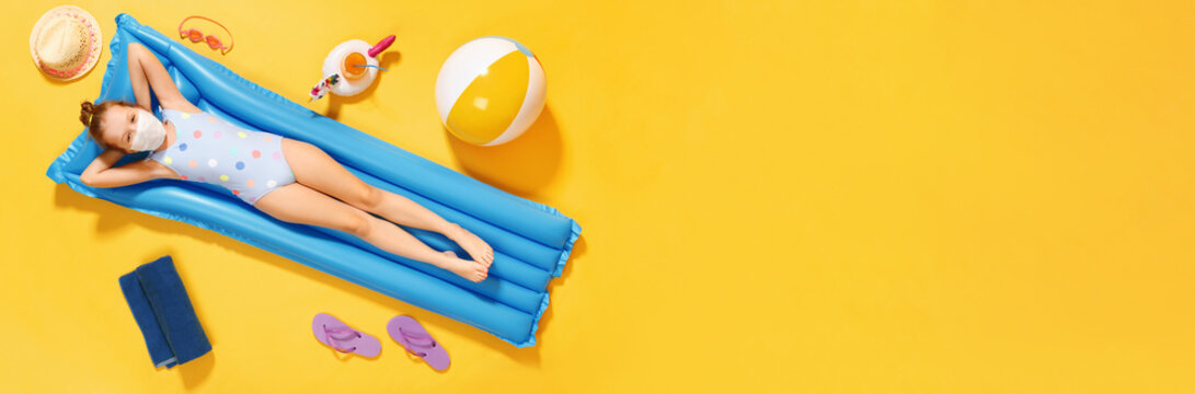 Top view on a little girl in a swimsuit and a protective mask resting on an inflatable blue mattress on a yellow background, concept of summer vacation. Banner copy space