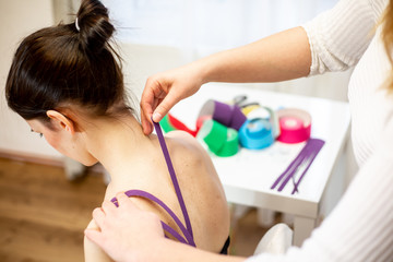 Female physiotherapist applying sport tape on the patient shoulder after her injury, healthcare concept