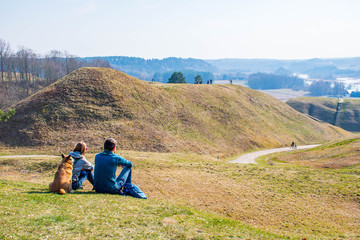 Fototapeta na wymiar Hills of Kernave, Lithuania, UNESCO world heritage, was a medieval capital of the Grand Duchy of Lithuania, tourist attraction and an archaeological site. Panorama of valley with couple and dog