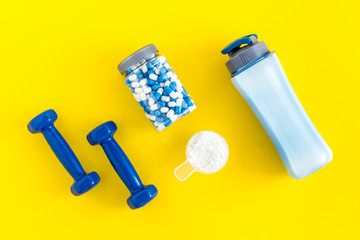 Creatine capsules, protein near shaker and dumbbells - sports supplements - flat lay on yellow...