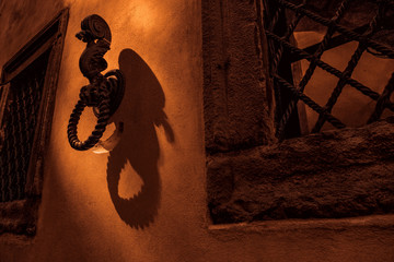 Door knocker on the wall with beautiful lights and shadows. Orange, bronze and gold colors. Copyspace concept. Some windows.