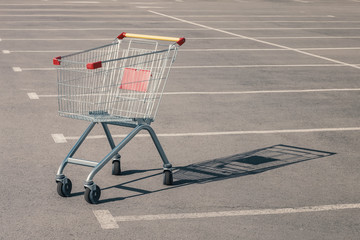 Empty grocery cart in an empty parking lot near a supermarket. Financial crisis, quarantine, lack of money concept