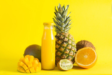Fototapeta na wymiar Fresh citrus juice in a glass bottle on a yellow background, pineapple, kiwi, coconut, orange, mango.