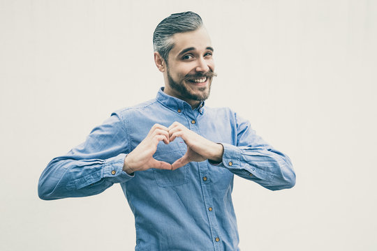 Positive Cheerful Man Making Heart With Hands. Grey Haired Young Man In Blue Casual Shirt Posing Isolated Over White Background. Love Gesture Concept