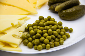 Beautiful green peas, cucumbers and sliced ​​cheese on white plate  against background. Keto diet with very healthy and tasty meal for luch