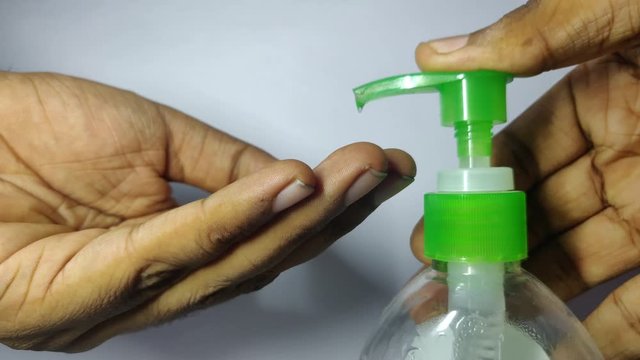 Indian Male hands pushing on Alcohol based Hand Sanitizer dispenser and squeeze out sanitizer gel on palm, closeup shot against white background.