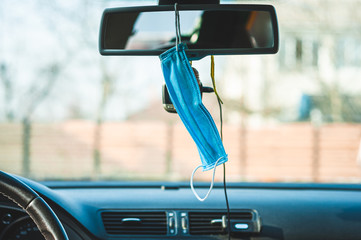 A blue medical antibacterial mask is hanging in the car's interior on a mirror in front of the DVR.