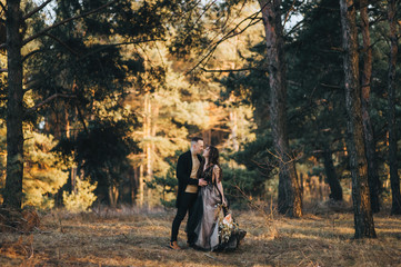 Loving groom and sweet bride in an expensive dress with long hair are hugging in the forest on the nature with pine trees. Wedding portrait of smiling newlyweds.