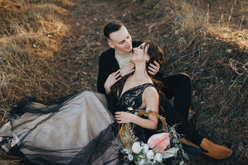 Loving groom in a black cardigan and a cute bride in an expensive dress are hugging, sitting in the...