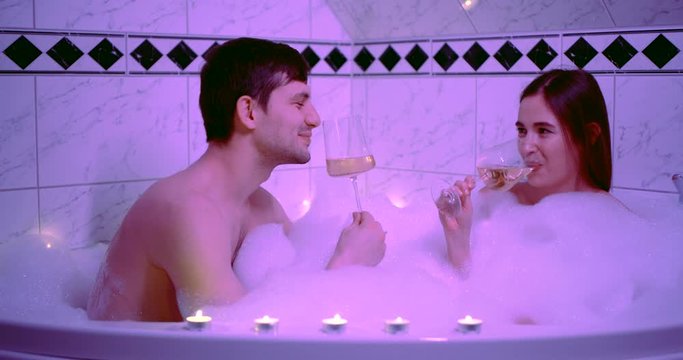 romantic date in bathroom with foam, man and woman are drinking wine and enjoying