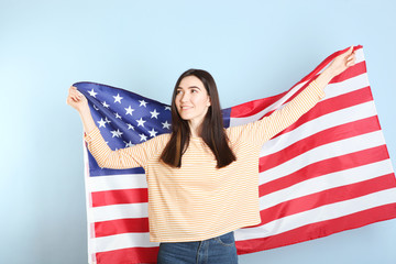 Beautiful young girl holding the flag of America on a colored background.