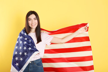 Beautiful young girl holding the flag of America on a colored background.