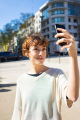 Fototapeta na wymiar Beautiful young woman taking selfie with smartphone. Cheerful young lady posing for self portrait on street. Self portrait concept