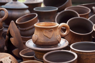 A cup of red clay with a heart. Sale at the fair a large number of diverse in style ceramic cups.