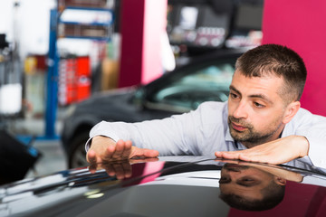Male client inspecting painting quality of vehicle