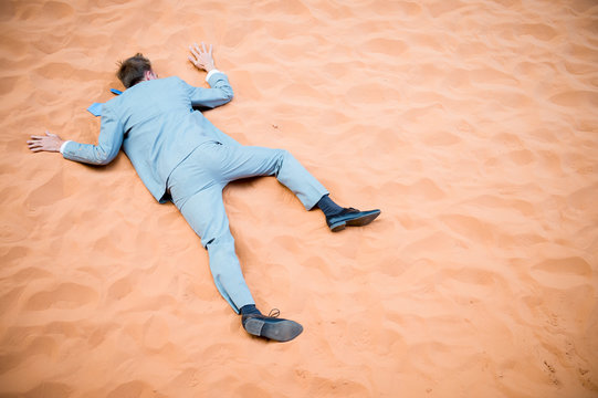 Unconscious businessman lying face down down collapsed on red sand desert background