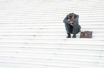 Depressed unrecognizable businessman hiding his face with his head in hands sitting outdoors on a large white staircase