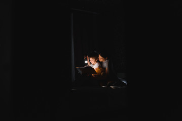Happy family. Time for stories. Delighted happy cute mother and son enjoying a book before sleeping and using a flashlight.