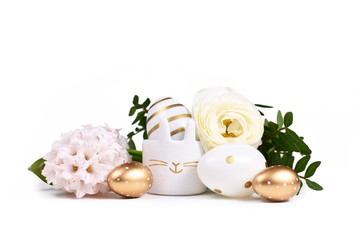 Painted Easter eggs with metallic golden and white stripes and dots and cute easter egg cup in shape of bunny surrounded by spring flowers on white background
