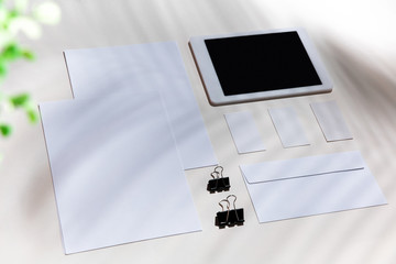 Sheets, gadgets and work tools on a white table indoors. Creative, cozy workplace at home office, inspirational mock up with plant shadows on surface. Concept of remote office, freelance, atmosphere.
