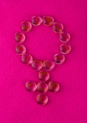 The symbol of the feminine laid out of small transparent stones on a pink background.