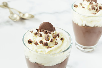 Chocolate mousse and cream cup for a restaurant menu with spoons on white marble background.