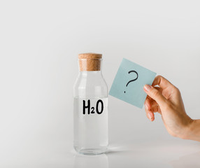Obraz premium Glass bottle with the inscription chemical formula of water on it and question mark on a note sheet.