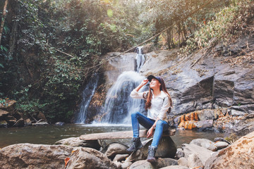 A beautiful asian woman sitting in front of waterfall in the jungle