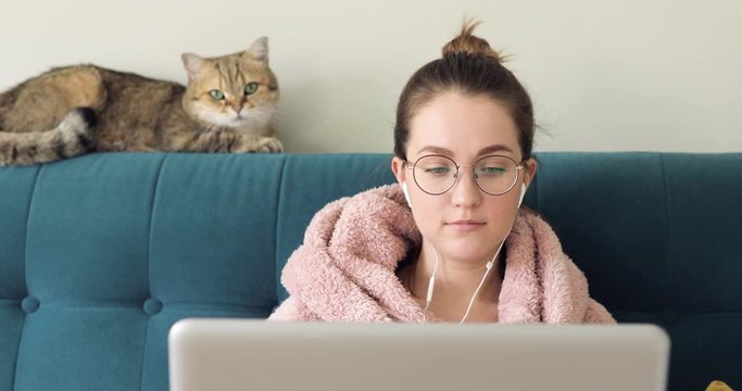 young woman sitting on couch using laptop notebook looking at screen typing message, webcam video call, chatting on computer browsing surfing internet social media studying or working online at home