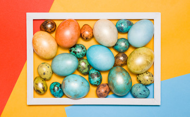 Colored Easter eggs in a wooden white frame on a colored background. Happy Easter!