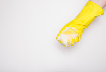 Hand in an yellow rubber glove with an yellow sponge and foam on a white background. Washing dishes, cleaning, home cleaning.