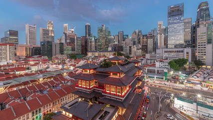 Obraz premium The Buddha Tooth Relic Temple comes alive at night in Singapore Chinatown day to night timelapse, with the city skyline in the background.