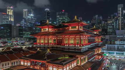 Obraz premium The Buddha Tooth Relic Temple comes alive at night timelapse in Singapore Chinatown, with the city skyline in the background.