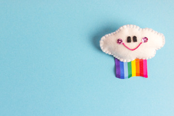 Nube sonriente con bandera arcoiris. Manualidad de fieltro sobre fondo celeste.
