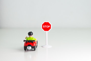 Coche de juguete parado frente a señal de tráfico de stop sobre fondo blanco.
