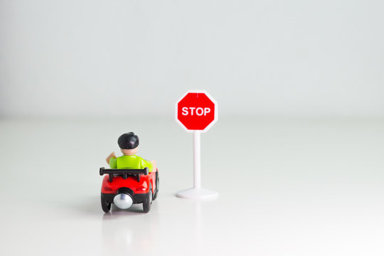 Coche de juguete parado frente a señal de tráfico de stop sobre fondo blanco.