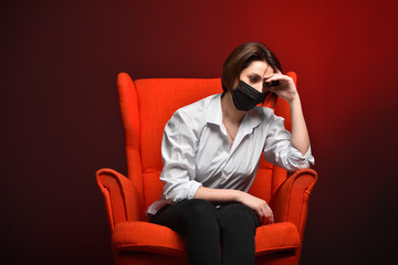 A stressed woman holds her head while sitting in a red chair, during a test and a coronavirus pandemic. The concept of viral danger and fear