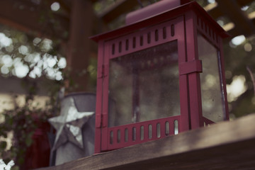 A closeup view of a rustic red candle lantern sitting on a patio ledge as decoration.
