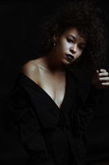 Beautiful afro american girl with curly hair posing in studio on dark background.
