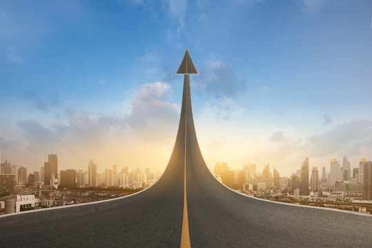 A road turning into an arrow rising upward on city background, symbolizing the direction to success in the future as a symbol of business vision.
