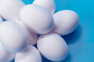 Whole white chicken eggs are lying on a blue background, close-up