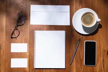 Gadgets, coffee, work tools on a wooden table indoors. Creative, cozy workplace at home office, inspirational mock up with plant shadows on surface. Concept of remote office, freelance, atmosphere.