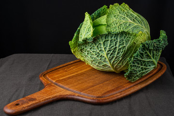 Close-up of green curly cabbage on wooden kitchen table and dark tablecloth, black background, horizontal and dark light