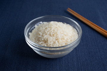 A side view of a glass bowl of short grain rice, with chopsticks on the side.