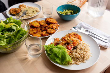 top view of healthy, fresh, organic homemade table spread with cooked salmon, green salad, guacamole, , rice and fried platano on wooden table with natural light