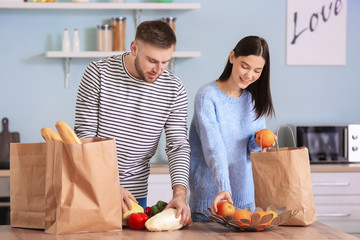 Young couple unpacking fresh products from market in kitchen