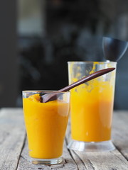 Two glasses of natural smoothie, juice, cocktail, made at home from the pulp of homemade pumpkin, on a blurred background of the kitchen.