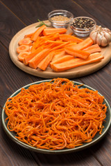 Fresh chopped carrots on cutting board. Fermented carrots in plate. Spices, garlic and parsley on table.