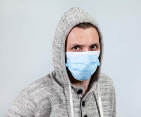 Scared Caucasian man in hood with one-use mask to protect him from virus. Covid-19 pandemic, grey background